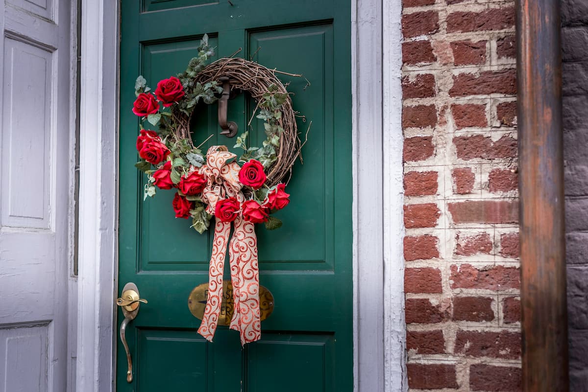 A Christmas wreath hanging on a green front door. There is red brickwork next to the door.